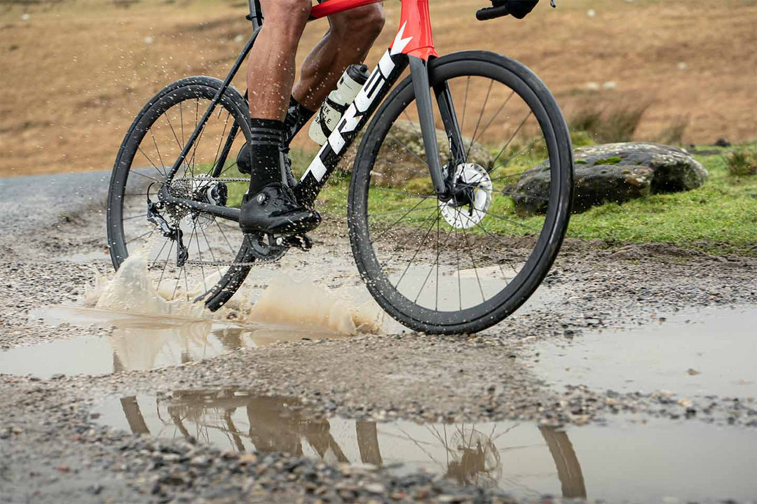 水たまりの水を跳ね上げながら走るロードバイクの足回りを撮影した写真