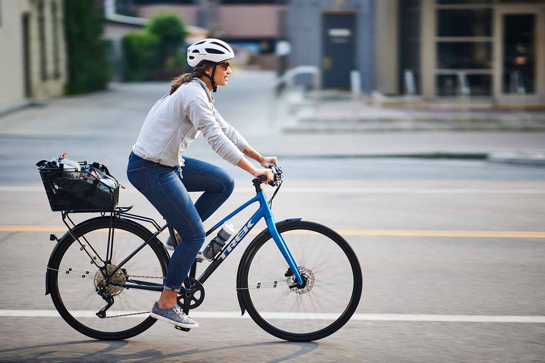 フェンダーやカゴをつけてクロスバイクで街を走る女性