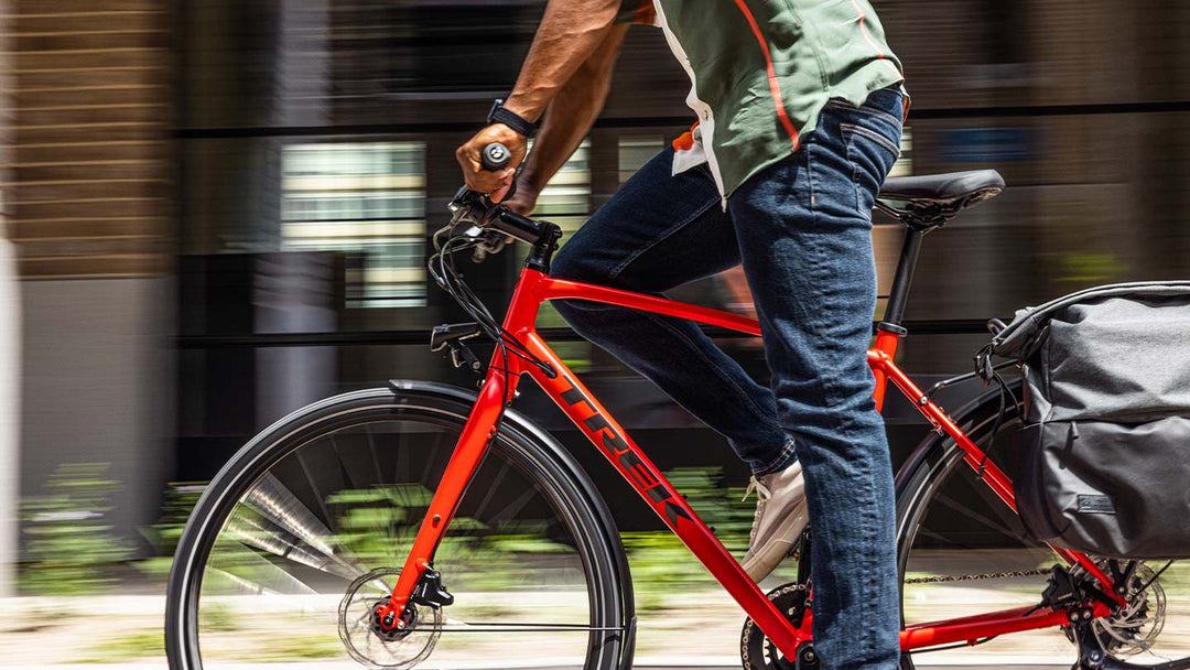 パニアバッグをつけた赤いクロスバイクを立ち漕ぎする男性の写真