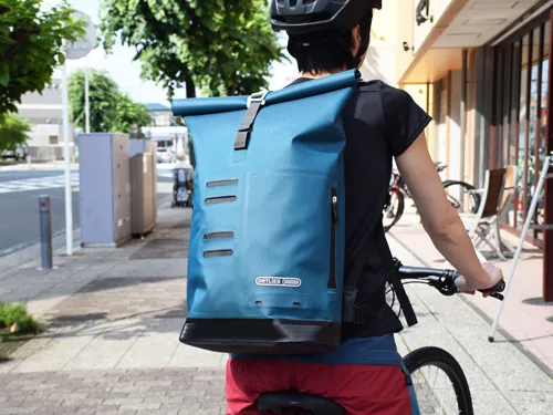 オルトリーブの防水コミューターバッグを背負ってクロスバイクにまたがった女性の写真