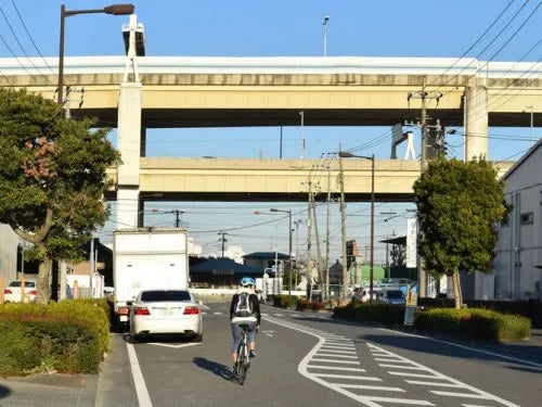 路上駐車している車をよけて車道を走るロードバイクを後ろから撮影