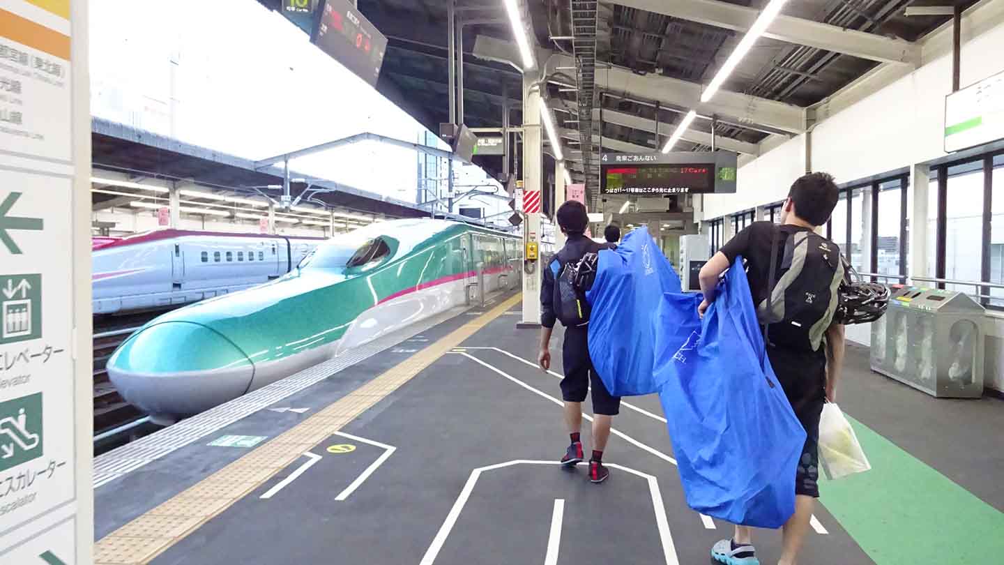 新幹線の駅のホームで輪行袋を担いでいる写真