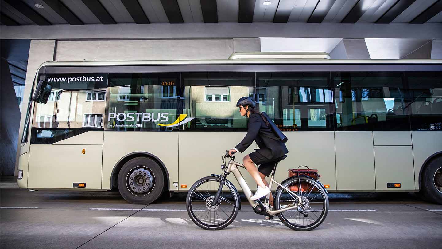 バスを横目にEバイクで出勤する海外女性の自転車通勤イメージ