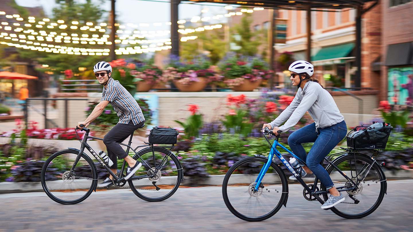 鮮やかなお花が沢山咲いている街角をクロスバイクでサイクリングしているカップルの写真。