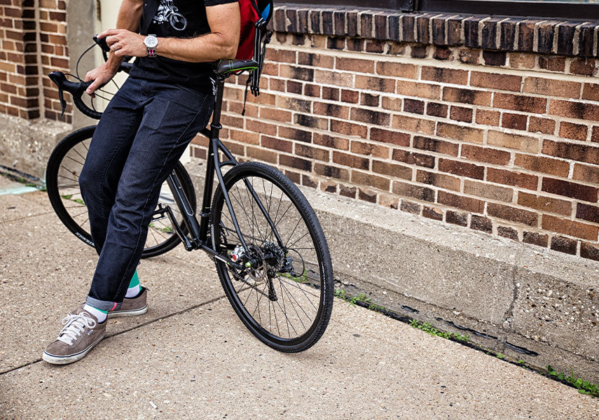 茶色いレンガの壁の前でロードバイクのトップチューブに腰をかけるサイクリストの写真