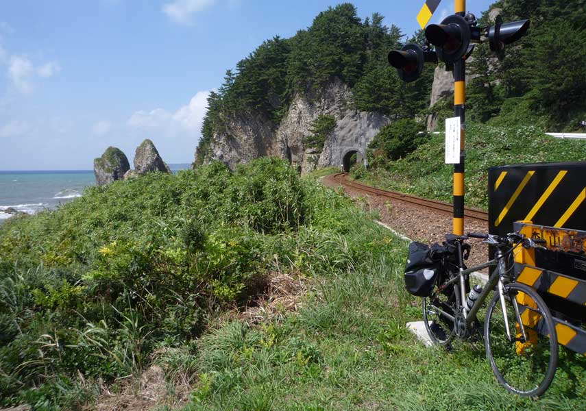 断崖絶壁と海を望む踏切にパニアバッグを取り付けたクロスバイクを立てかけた写真