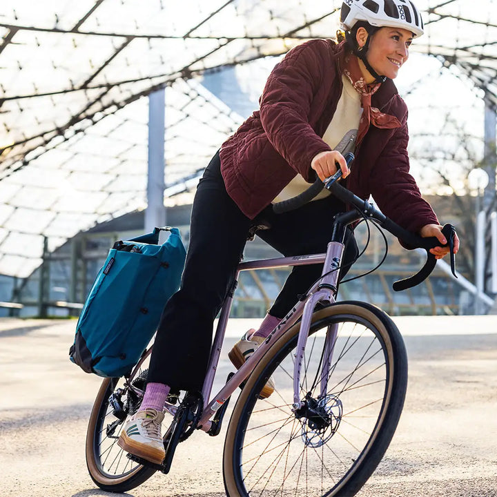 Ortlieb（オルトリーブ）Vario Lite（ヴァリオライト）カラー：ぺトロール　リアキャリアに付けてロードバイクを走行する女性